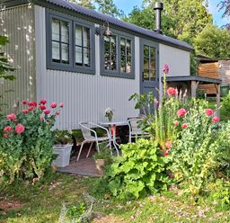 A garden with flowers and seating near a small building at Evendine Hut @ Evendine Cottage, Colwall, Herefordshire