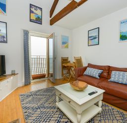 A living room with a leather sofa pillows coffee table and balcony door showing ocean view at 2 Bayview in Torcross