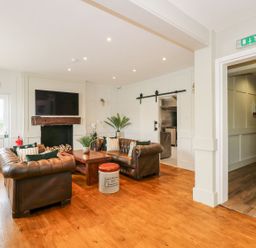 A seating area with brown leather sofas coffee table and a television above a fireplace at The Five Bells Inn in Upwell