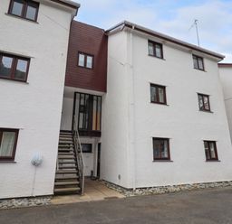 Exterior view of a white multi-story apartment building with brown framed windows and an outdoor staircase at 9 Oakley Wharf in Porthmadog