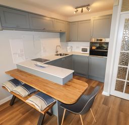 A kitchen with grey cabinets a wooden dining table with cushions on benches and a grey chair at 9 Oakley Wharf in Porthmadog