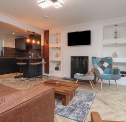 A living room with a brown leather sofa a wooden coffee table a patterned armchair a fireplace and a mounted TV at Sea Cliff in Morfa Nefyn