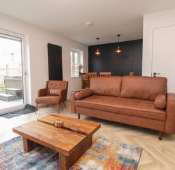 A living room with a brown sofa a brown armchair a wooden coffee table colorful rug and dining area at Sea Cliff in Morfa Nefyn
