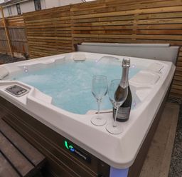 An outdoor hot tub with bubbling water two empty wine glasses and a bottle of prosecco on the edge near a wooden fence at Sea Cliff in Morfa Nefyn