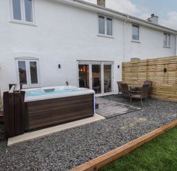 An outdoor area with a hot tub table and chairs fenced yard at Sea Cliff in Morfa Nefyn