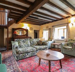 A living room with floral and striped armchairs a wooden coffee table and a red patterned rug at The Long House in Penmachno