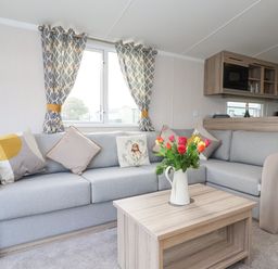 A living room with a grey sectional sofa cushions and a wooden coffee table with flowers at Lazy Dayz Lodge in East Heslerton near Malton