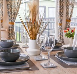 A dining table set with dark gray bowls and plates wine glasses and a white vase with dried plants at Lazy Dayz Lodge East Heslerton near Malton