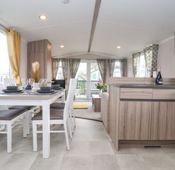 A dining area with a table set with glasses and plates next to a kitchen with wooden cabinets at Lazy Dayz Lodge in East Heslerton near Malton
