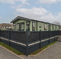 A green mobile home with multiple windows and a black railing deck on a gravel and grass lot at Lazy Dayz Lodge in East Heslerton near Malton