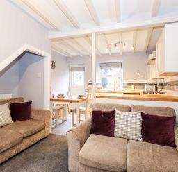 A living room with two sofas and pillows next to a dining area with a wooden table and chairs and an open kitchen with wooden countertops at Fell View in Ambleside
