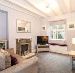 A living room with a stone fireplace television on a wooden stand and a window seat at Fell View in Ambleside
