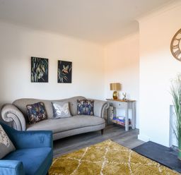 A living room with a sofa armchair cushions side table wall clock and decorative plants at Hook Farm Cottage in Uplyme