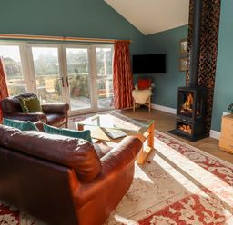 A living room with leather sofa and armchair glass coffee table wood burning stove and large windows at Summerseats Cottage in Alnwick