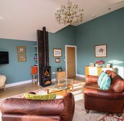 A living room with leather sofas a wood burning stove a glass coffee table and a chandelier at Summerseats Cottage in Alnwick