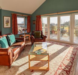 A living room with leather sofa and armchair glass coffee table and large windows at Summerseats Cottage in Alnwick