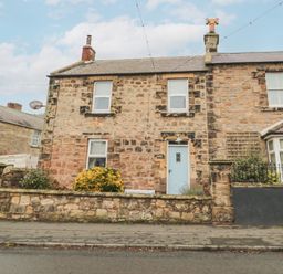 A stone house with a blue door and three windows behind a low stone wall at The Haven in North Sunderland near Seahouses