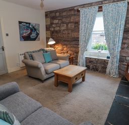 A living room with sofas a wooden coffee table and stone wall at The Haven in North Sunderland near Seahouses