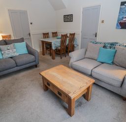 A living room with two sofas a wooden coffee table a dining table with chairs and paintings on the walls at The Haven in North Sunderland near Seahouses