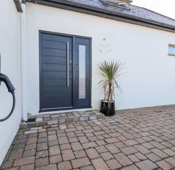 A paved outdoor area with a dark blue door a potted plant and an electric vehicle charger on a white wall at Little Beach Cabin in Crantock
