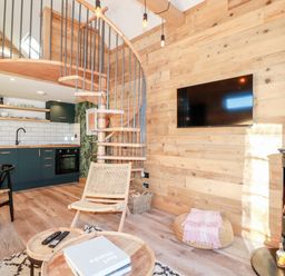 A living area with a wooden spiral staircase kitchen cabinets and a wood burning stove at Little Beach Cabin in Crantock