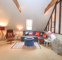 A living room with a gray sectional sofa a blue ottoman a brown recliner and decorative lamps at The Hayloft in Haddiscoe