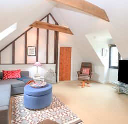 An attic living room with a gray sectional sofa and colorful pillows and a blue ottoman on a patterned rug at The Hayloft in Haddiscoe