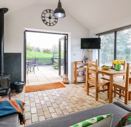 A living area with wooden dining table and chairs a wood stove and open patio doors at The Grain Store in Haddiscoe