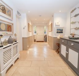 A hallway with beige floor tiles white paneled walls a gray and white cabinet on the right and a white radiator cover on the left at Lampland House in Walberswick
