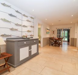 A hallway with a gray and white cabinet wall art of fish and a dining table with chairs at Lampland House in Walberswick