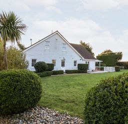 A white house with a pitched roof surrounded by a lawn and bushes at Lampland House in Walberswick
