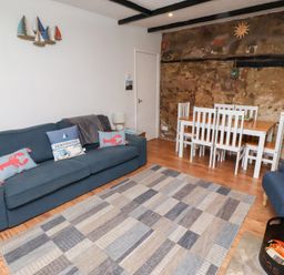 A living room with a blue sofa a dining table with white chairs and a patterned rug at Seascape Cottage in Seahouses