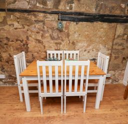 A dining area with a wooden table and five white chairs against a stone wall at Seascape Cottage in Seahouses
