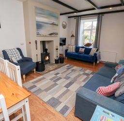 A living room with two blue sofas a blue armchair a wood burning stove and a wooden dining table at Seascape Cottage in Seahouses