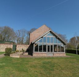 A brick building with large glass windows and a pitched roof in a grassy yard with trees at The Barn Helperby near Boroughbridge