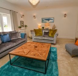 A living room with two sofas a patterned armchair a wooden coffee table and a teal rug at Hindon Hall in Lelant near Carbis Bay