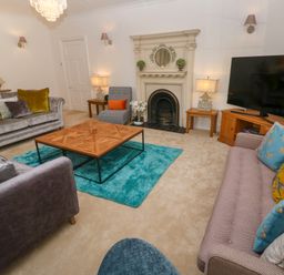 A living room with sofas a wooden coffee table a fireplace a large television and lamps at Hindon Hall in Lelant near Carbis Bay
