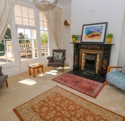 A living room with armchairs rugs a fireplace and large windows at Hindon Hall in Lelant near Carbis Bay