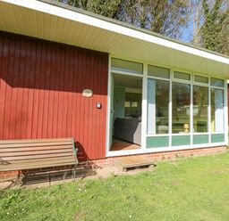 The exterior of a red wooden building with a bench and an open door showing a living area at The Beach Hut in Cromer