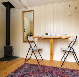 A small dining area with a wooden wall mounted table two folding chairs a wood stove and a mirror at Mitford Gypsy Hut in Moreton-In-Marsh