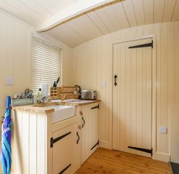 A small kitchen corner with a sink, dish rack, toaster, and an umbrella leaning against the counter at Mitford Gypsy Hut in Moreton-In-Marsh
