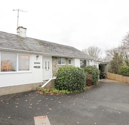 The exterior of a single-story house with a white front door bushes in front and a paved driveway at 15 Maes Awel in Abersoch