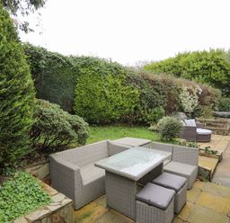 An outdoor patio area with a wicker dining set including a table and chairs surrounded by greenery at 15 Maes Awel in Abersoch