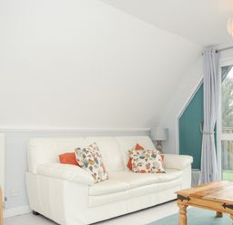 A living room with a white sofa with floral cushions a wooden coffee table two lamps and a sliding glass door at 24 Valley Lodge in Honicombe Park near Drakewalls