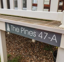 A porch with a wood deck and a sign reading The Pines 47-A at Evergreen Pines in Cayton Bay near Scarborough