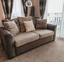 A sofa with cushions near windows with blinds and patterned curtains at Evergreen Pines in Cayton Bay near Scarborough