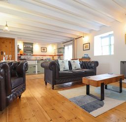 A living room with leather couches and a wooden coffee table next to a kitchen area at Oofoo's Barn in Mullion