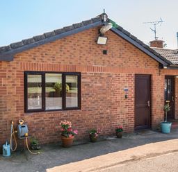 An exterior view of a brick house with flower pots at Piglet Corner in Culmstock