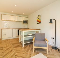 A kitchen with white cabinets a wooden countertop a gray armchair a black floor lamp and a framed picture on the wall at Valise in Bideford