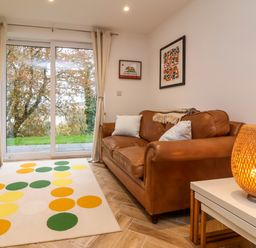 A living room with a brown leather sofa two white pillows a patterned rug and a wicker lamp on a table at Valise in Bideford